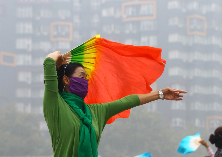 2014年10月9日上午,河南郑州,一名晨练的女士在戴着口罩跳扇子舞。